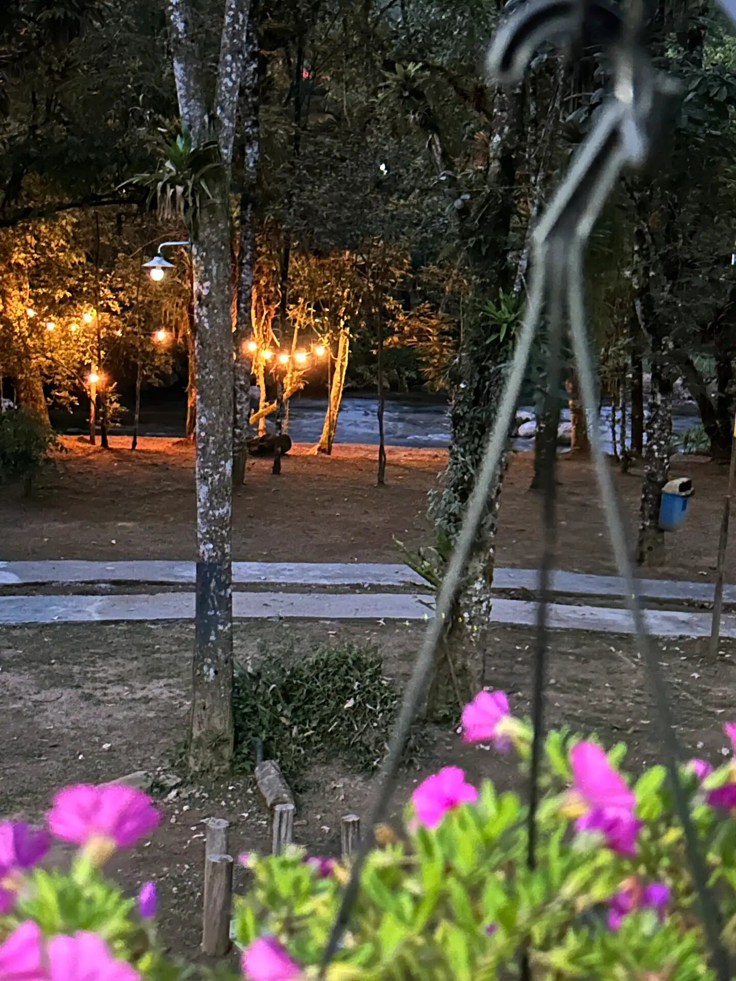 Área externa iluminada por luzes amarelas à beira do rio ao entardecer